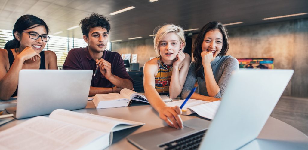 College students using laptop while sitting at table. Group study for school assignment.