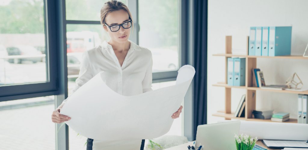 Creative brown haired serious focused concentrated lady is doing paper work, nice interior, huge windows, shelves with folders, perfect work station. Remodeling, visual art design, tone, web